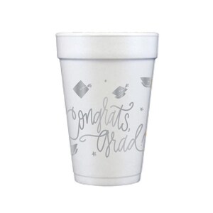 Puede incluir: Un vaso de espuma blanco con texto plateado y gr&aacute;ficos de gorros de graduaci&oacute;n. El vaso presenta las palabras "Congrats Grad" en una fuente de escritura, junto con peque&ntilde;as ilustraciones de estrellas y birretes. Ideal para celebraciones de graduaci&oacute;n.