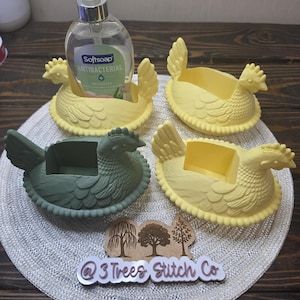 May include: Three yellow and one dark green chicken-shaped holders with textured feather details. One yellow holder contains a clear plastic bottle of Softsoap Antibacterial soap. A wooden sign with three tree icons and the text @3 Trees Stitch Co.