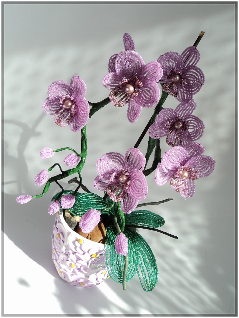 May include: A bouquet of purple beaded orchids in a white ceramic pot with a floral pattern. The orchids are made of small beads and have a realistic appearance.