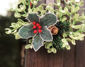 May include: A beaded Christmas wreath with green leaves, red berries, and a gold accent. The wreath is made of small beads and is a festive decoration.