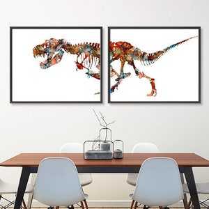 Może przedstawiać: Dwa oprawione wydruki artystyczne przedstawiające kolorowe ilustracje szkielet&oacute;w dinozaur&oacute;w. Grafika przedstawia T-Rexa w żywym stylu akwarelowym, z mieszanką czerwonych, niebieskich i ż&oacute;łtych odcieni. Wydruki są prezentowane na białej ścianie nad drewnianym stołem.