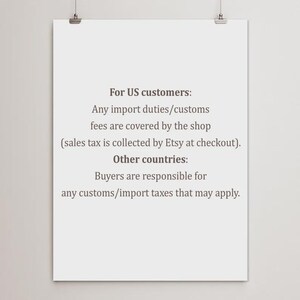 Może przedstawiać: Biały plakat z czarnym tekstem wisi na dw&oacute;ch srebrnych klipsach. Tekst zawiera informacje o cłach importowych i opłatach celnych dla klient&oacute;w z USA i innych kraj&oacute;w.