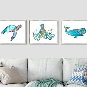 May include: Three framed watercolor prints featuring sea creatures: a sea turtle, an octopus, and a whale. The artwork uses shades of blue, green, and yellow against a white background. The prints are displayed above a white couch.
