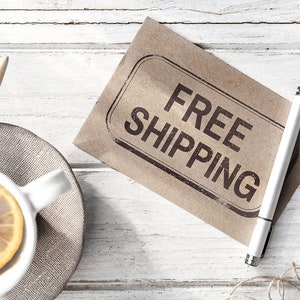 May include: A brown paper envelope with the words "FREE SHIPPING" stamped in black ink. A white pen is lying on top of the envelope.