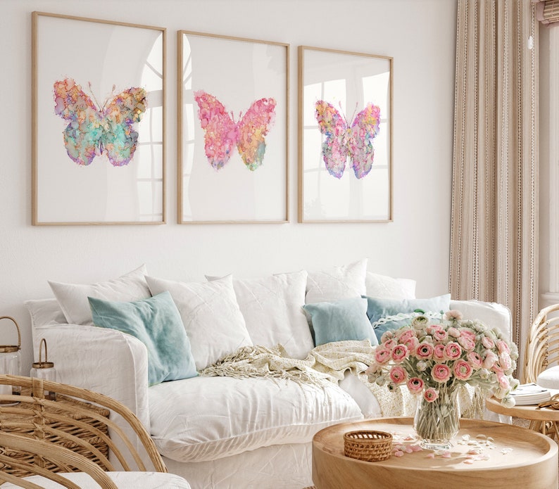 May include: Three framed watercolor paintings of butterflies with pink, blue, and purple hues. The butterflies are set against a white background.