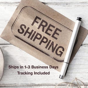May include: A brown paper tag with the words "FREE SHIPPING" in large, bold, black letters. A white pen rests on the tag. The background is a white, weathered wood surface.
