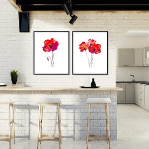 May include: Two framed watercolour paintings of red poppies on a white background. The paintings are hanging on a white brick wall above a wooden countertop.