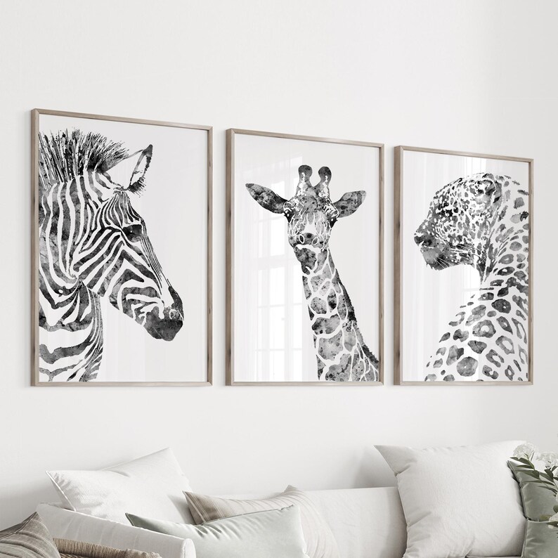 K&ouml;nnte beinhalten: Ein Set aus drei gerahmten Wandbildern mit schwarz-wei&szlig;en Aquarellillustrationen eines Zebras, einer Giraffe und eines Leoparden. Jedes Tier ist im Profil oder von vorne vor einem schlichten wei&szlig;en Hintergrund in d&uuml;nnen Holzrahmen dargestellt.