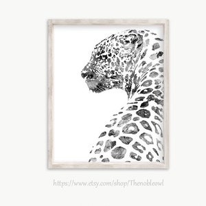 K&ouml;nnte beinhalten: Ein gerahmter Kunstdruck mit einer schwarz-wei&szlig;en Aquarellillustration eines Leoparden im Profil, der nach links blickt. Der Leopard hat detaillierte dunkle Flecken auf wei&szlig;em Hintergrund und ist in einem hellen Holzrahmen gefasst.