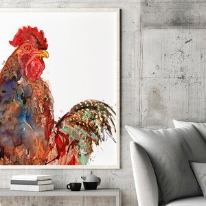 May include: Watercolor painting of a rooster in a white frame. The rooster has red, brown, blue, and green feathers. The artwork is displayed on a gray shelf with books, a teapot, and cups. The background is a gray concrete wall.
