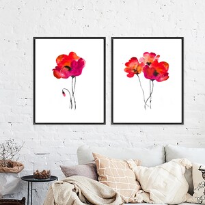 May include: Two framed watercolour paintings of red poppies on a white background. The paintings are in black frames and are hung on a white brick wall.