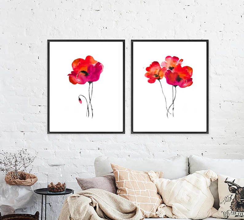 May include: Two framed watercolour paintings of red poppies on a white background. The paintings are in black frames and are hung on a white brick wall.