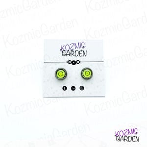 A pair of green and black spirit level bubble earrings. The earrings are round and have a silver metal backing.