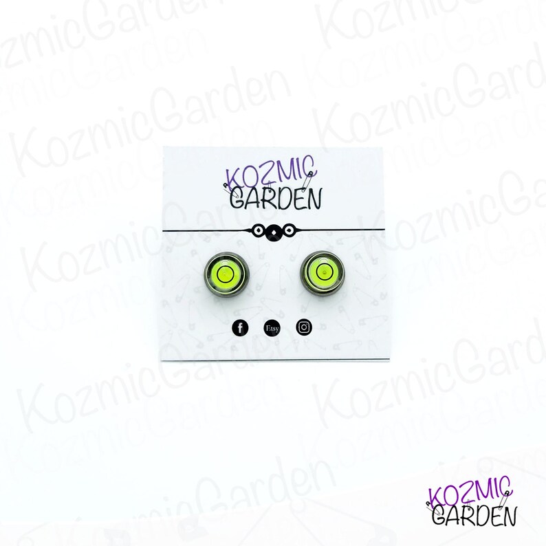 A pair of green and black spirit level bubble earrings. The earrings are round and have a silver metal backing.