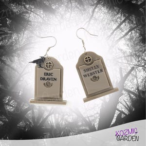 Puede incluir: Un par de pendientes de plata con forma de lápida con detalles de cuervo negro. El pendiente izquierdo dice "ERIC DRAVEN" y el pendiente derecho dice "SHELLY WEBSTER".