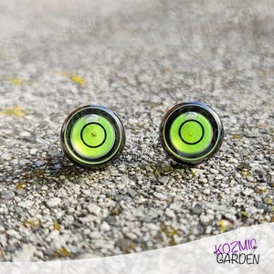 A pair of green and black spirit level bubble earrings. The earrings are round and have a silver metal backing.