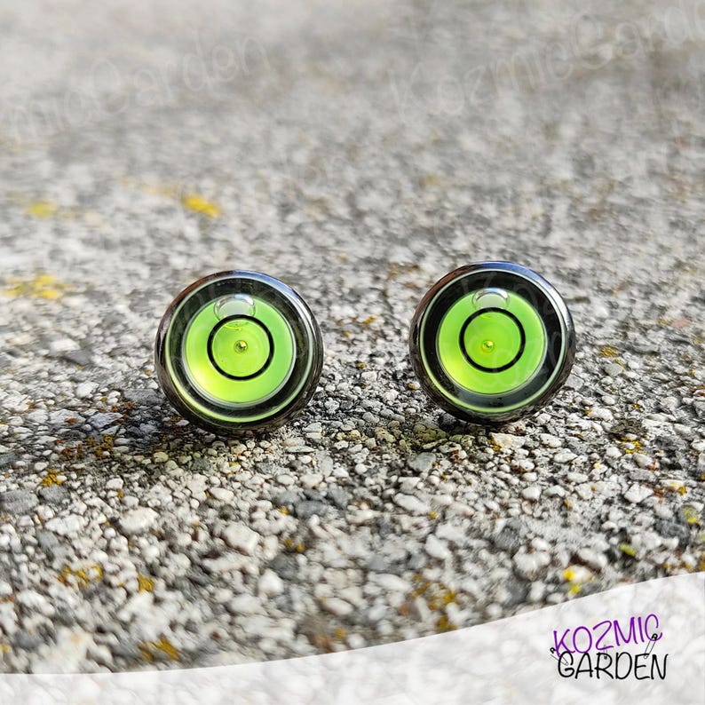A pair of green and black spirit level bubble earrings. The earrings are round and have a silver metal backing.