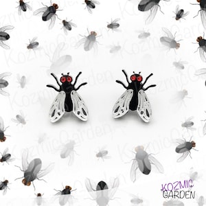 May include: A pair of black and silver fly-shaped earrings with red accents. The earrings are set against a white background with a pattern of smaller fly illustrations. The earrings are a unique accessory.