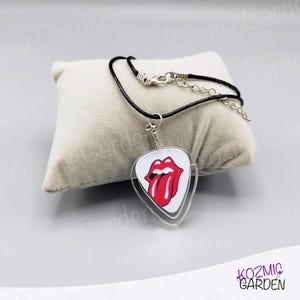 May include: A black cord necklace with a clear, guitar pick-shaped pendant. The pendant features a white background with the iconic red lips and tongue logo. The necklace has a silver clasp.