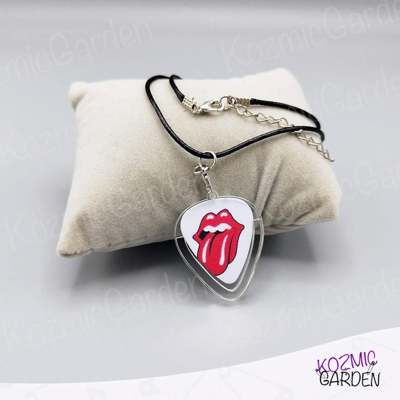 May include: A black cord necklace with a clear, guitar pick-shaped pendant. The pendant features a white background with the iconic red lips and tongue logo. The necklace has a silver clasp.
