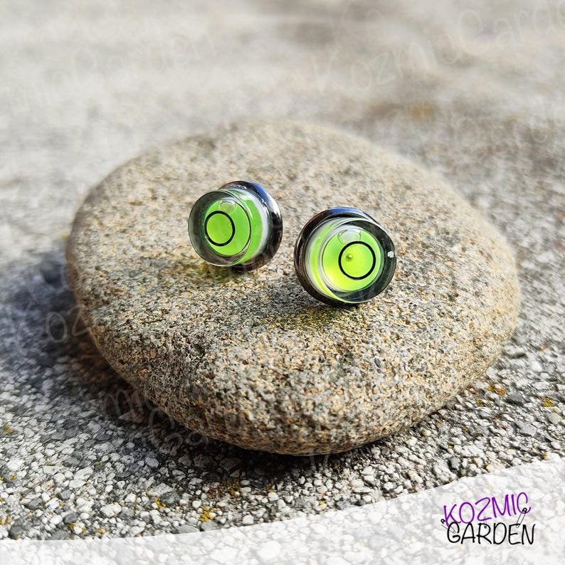 A pair of green and black spirit level bubble earrings. The earrings are round and have a silver metal backing.