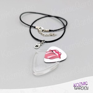 May include: A white guitar pick pendant featuring a pink lips design, a clear plastic pick holder, and a black cord necklace with a silver clasp. A distinctive accessory.