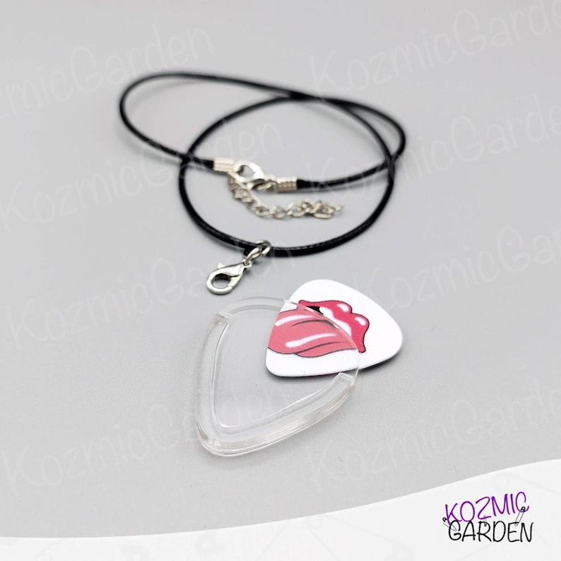 May include: A white guitar pick pendant featuring a pink lips design, a clear plastic pick holder, and a black cord necklace with a silver clasp. A distinctive accessory.