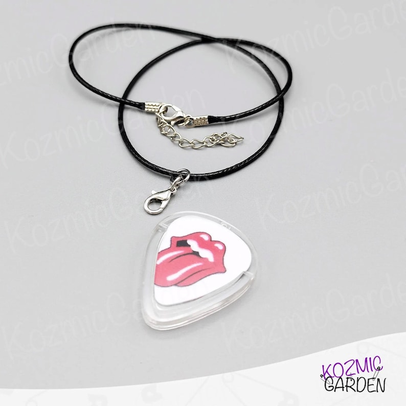 May include: A black cord necklace with a silver clasp and a guitar pick pendant. The pendant has a white background and a pink tongue and lips graphic.
