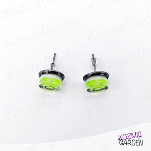A pair of green and black spirit level bubble earrings. The earrings are round and have a silver metal backing.