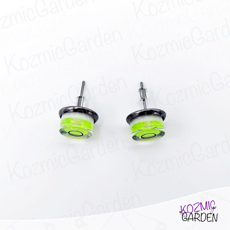 A pair of green and black spirit level bubble earrings. The earrings are round and have a silver metal backing.