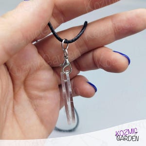 May include: Clear acrylic pendant necklace with a black cord. The pendant has a layered rectangular design. The necklace features a silver-coloured clasp and ring. The background is a light grey.