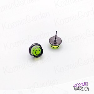 A pair of green and black spirit level bubble earrings. The earrings are round and have a silver metal backing.