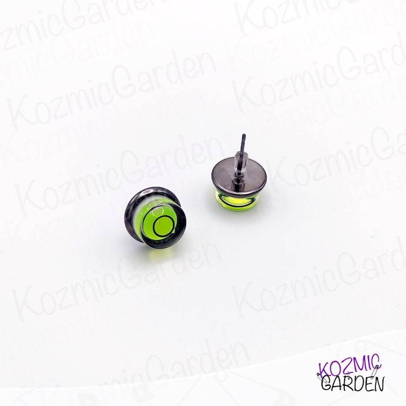 A pair of green and black spirit level bubble earrings. The earrings are round and have a silver metal backing.