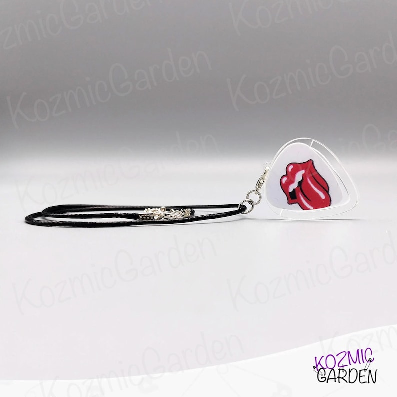 May include: A clear, guitar pick-shaped pendant with the famous red lips logo. It hangs from a black cord necklace with a silver-coloured clasp. The design is a tribute to rock music.
