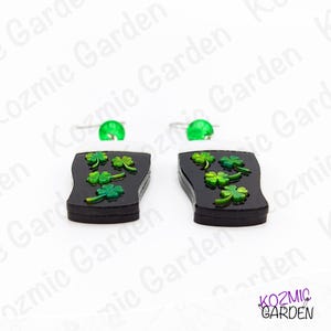 May include: A pair of black earrings shaped like a pint of stout, with green shamrocks and a white foam top. Each earring has a green bead at the top and a silver hook. The earrings are from Kozmic Garden.