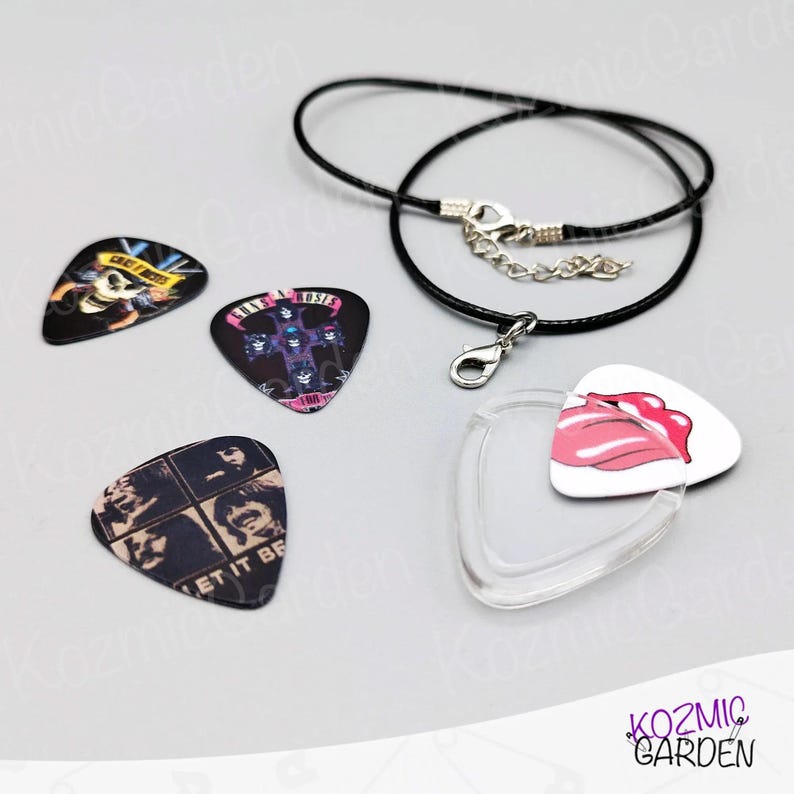 May include: A selection of guitar plectrums with band logos and a Rolling Stones tongue design. Includes a black cord necklace with a clasp and a clear pick holder. The plectrums feature various colours and designs.