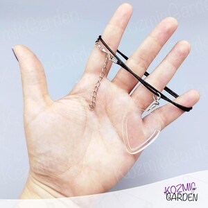 May include: Clear heart-shaped pendant necklace with a black cord and silver-coloured chain. The pendant is transparent and has a smooth surface. The necklace is displayed against a light grey background.
