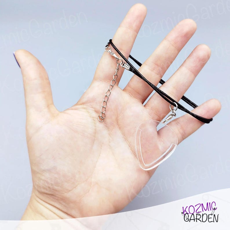 May include: Clear heart-shaped pendant necklace with a black cord and silver-coloured chain. The pendant is transparent and has a smooth surface. The necklace is displayed against a light grey background.