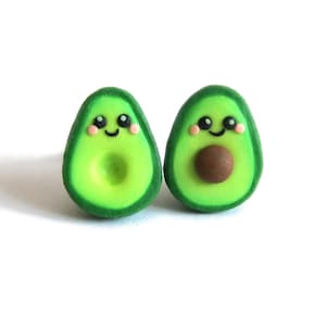 Può includere: Un paio di orecchini a forma di avocado con facce carine. Gli orecchini sono fatti di pasta polimerica verde, marrone e rosa.