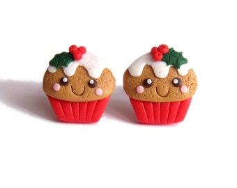 May include: A pair of red and brown Christmas cupcake earrings with white frosting and green holly accents. The cupcakes have a smiling face.