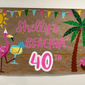 May include: A hand-painted banner with a beach theme. The banner features a pink flamingo, a cocktail, a palm tree, and the words "Shelly's Beachin' 40th" in pink lettering. Colorful confetti and a sun are also included.