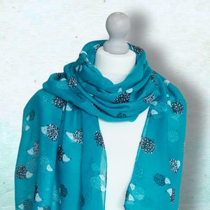 May include: A teal scarf featuring a repeating pattern of white and black hedgehogs. The scarf is draped over a white mannequin. The fabric is lightweight and flowing, ideal for spring or summer.