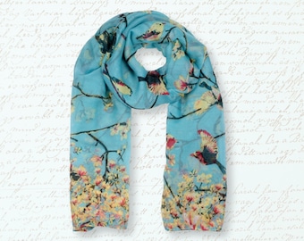 May include: A light blue scarf with a floral and bird print. The scarf features a repeating pattern of pink and yellow flowers and blue birds on a light blue background.