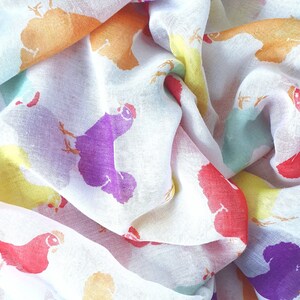 May include: A white sheer scarf with a colorful chicken print. The chickens are in various colors, including red, orange, yellow, green, purple, and blue.