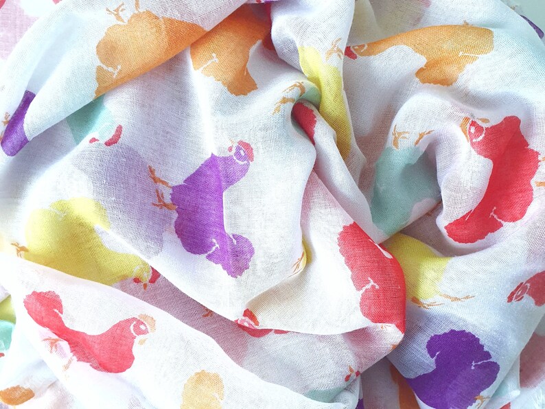 May include: A white sheer scarf with a colorful chicken print. The chickens are in various colors, including red, orange, yellow, green, purple, and blue.