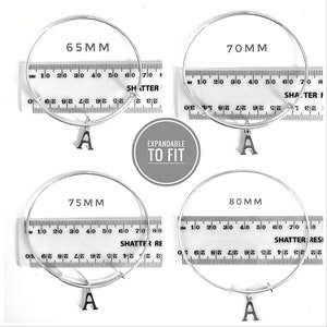 May include: Four silver expandable bangle bracelets with a letter 'A' charm. The bracelets are measured in millimeters: 65mm, 70mm, 75mm, and 80mm.
