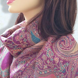 May include: A pink and teal paisley patterned scarf with a fringed edge.