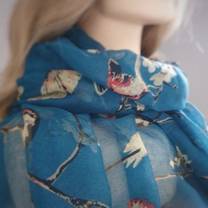 May include: A teal blue scarf with a white and red bird print.