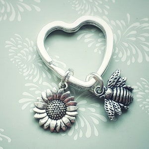 May include: A silver heart-shaped keyring with a silver sunflower charm and a silver bee charm.