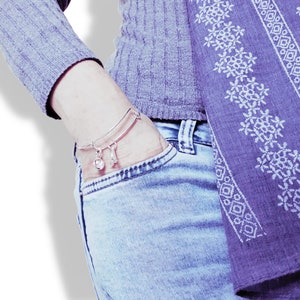 May include: A silver charm bracelet with a bell and a bone charm. The bracelet is worn on a person's wrist, and the person is wearing a gray sweater and blue jeans.